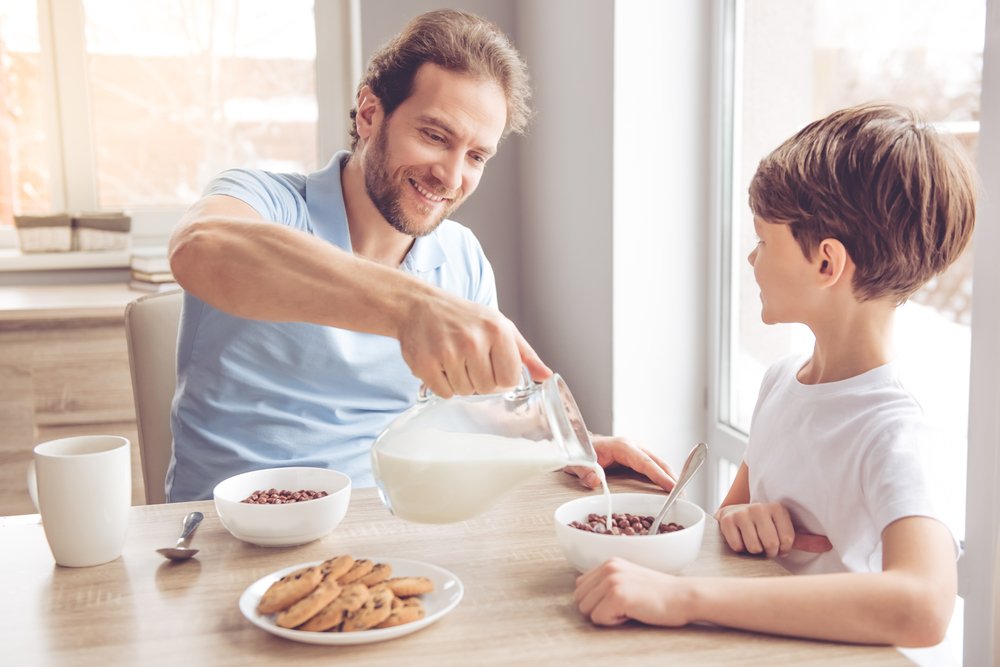 Father and son are smiling while having a breakfast in kitchen