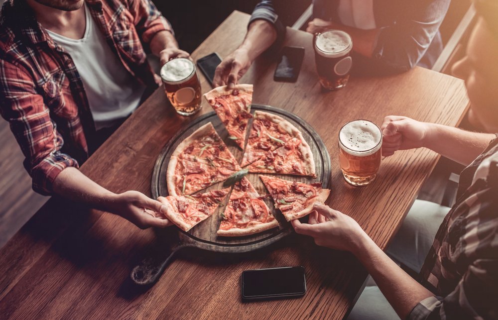 friends in bar are drinking beer and eating pizza