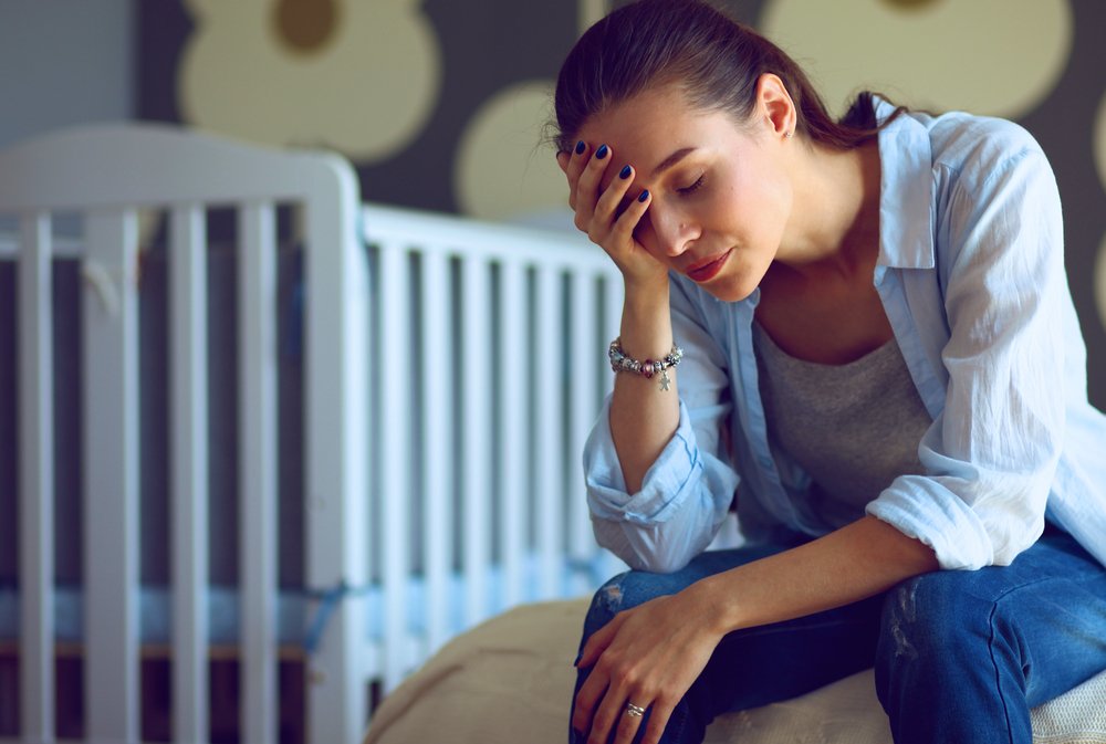 tired woman sitting on the bed near children's cot